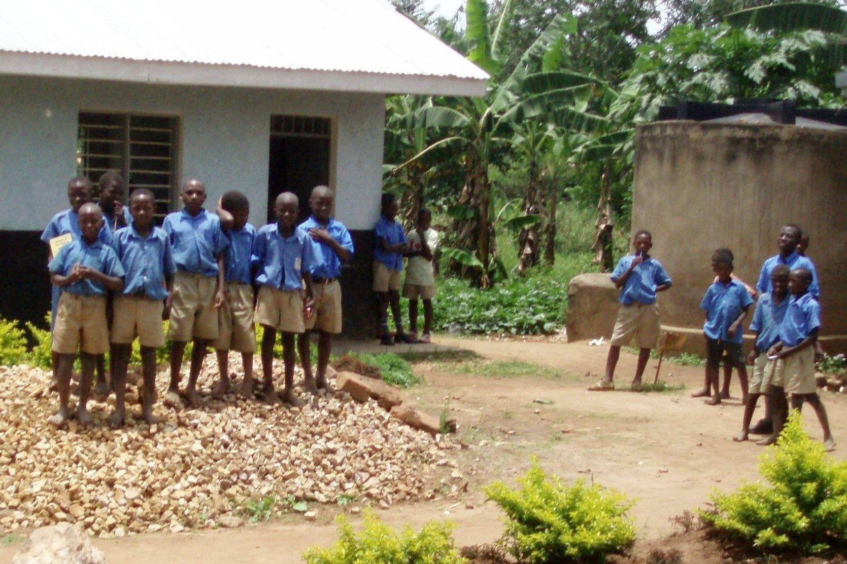 Ugandische männliche Schüler vor Schulgebäude mit neuem Wassertank