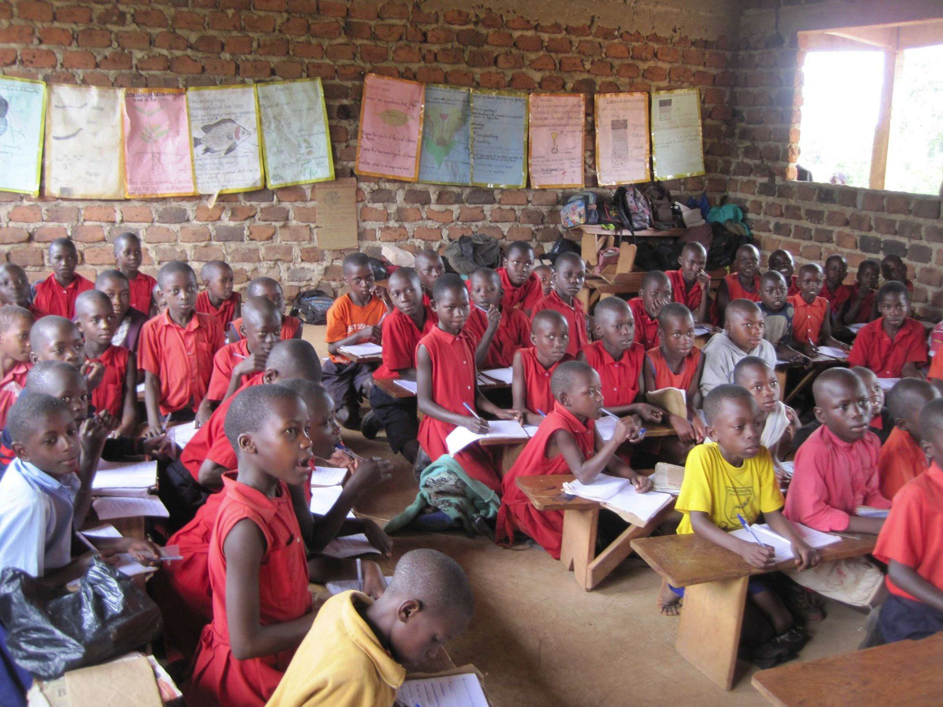 Ugandische Schulkinder mit überwiegend roter Kleidung in gemauertem Schulzimmer